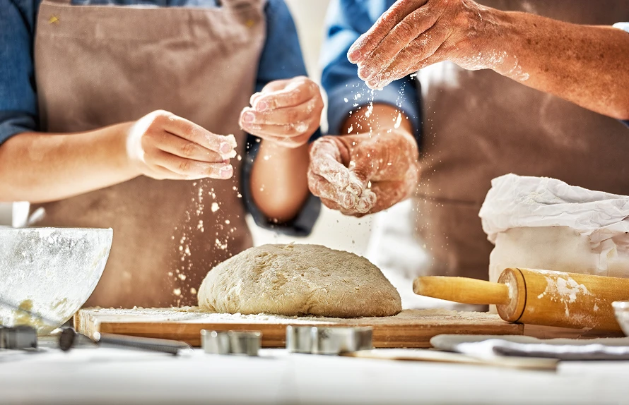 two bakers sprinkling flour on a loaf of artisan bread